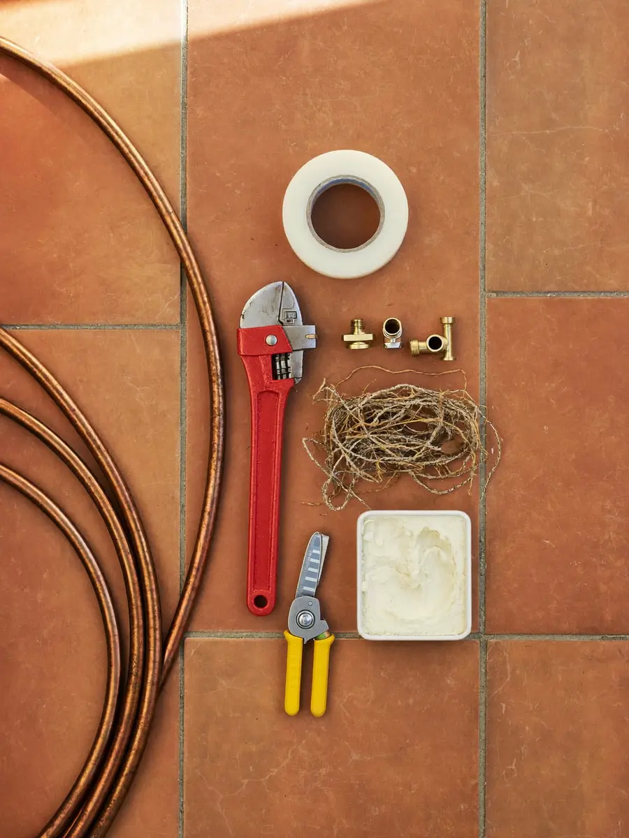 Clé à molette, tube de cuivre et raccords en laiton posés sur un carrelage